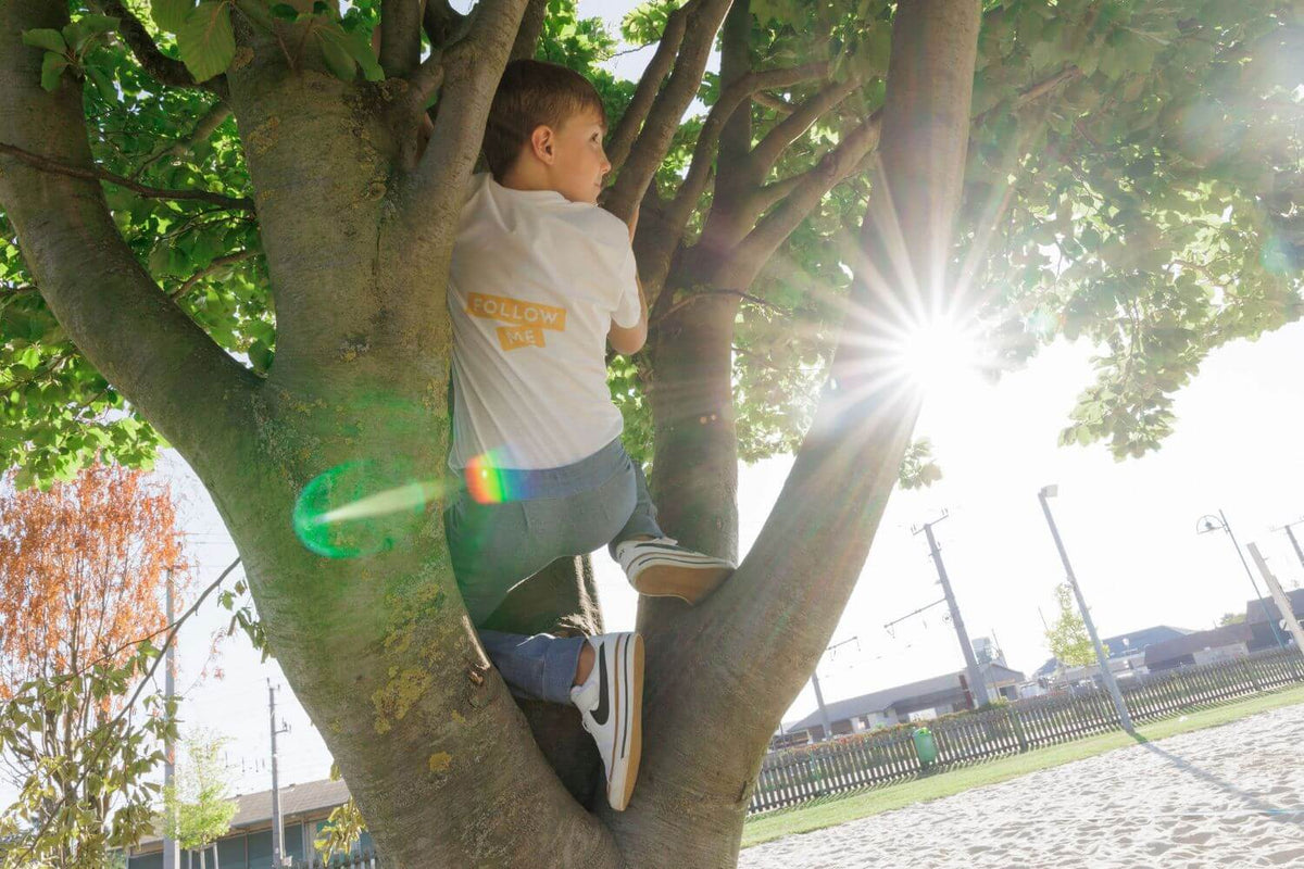 nachhaltige kinderkleidung bio baumwolle babbily. junge klettert ein baum, trägt eine nachhaltige hose aus bio baumwolle mit verstärktem knie